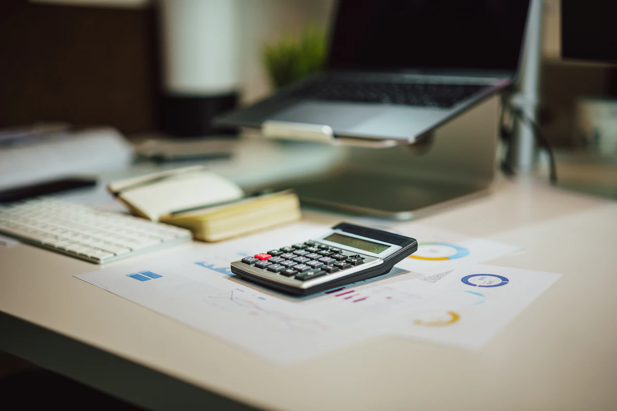 A calculator on a desk next to a laptop and printed charts.