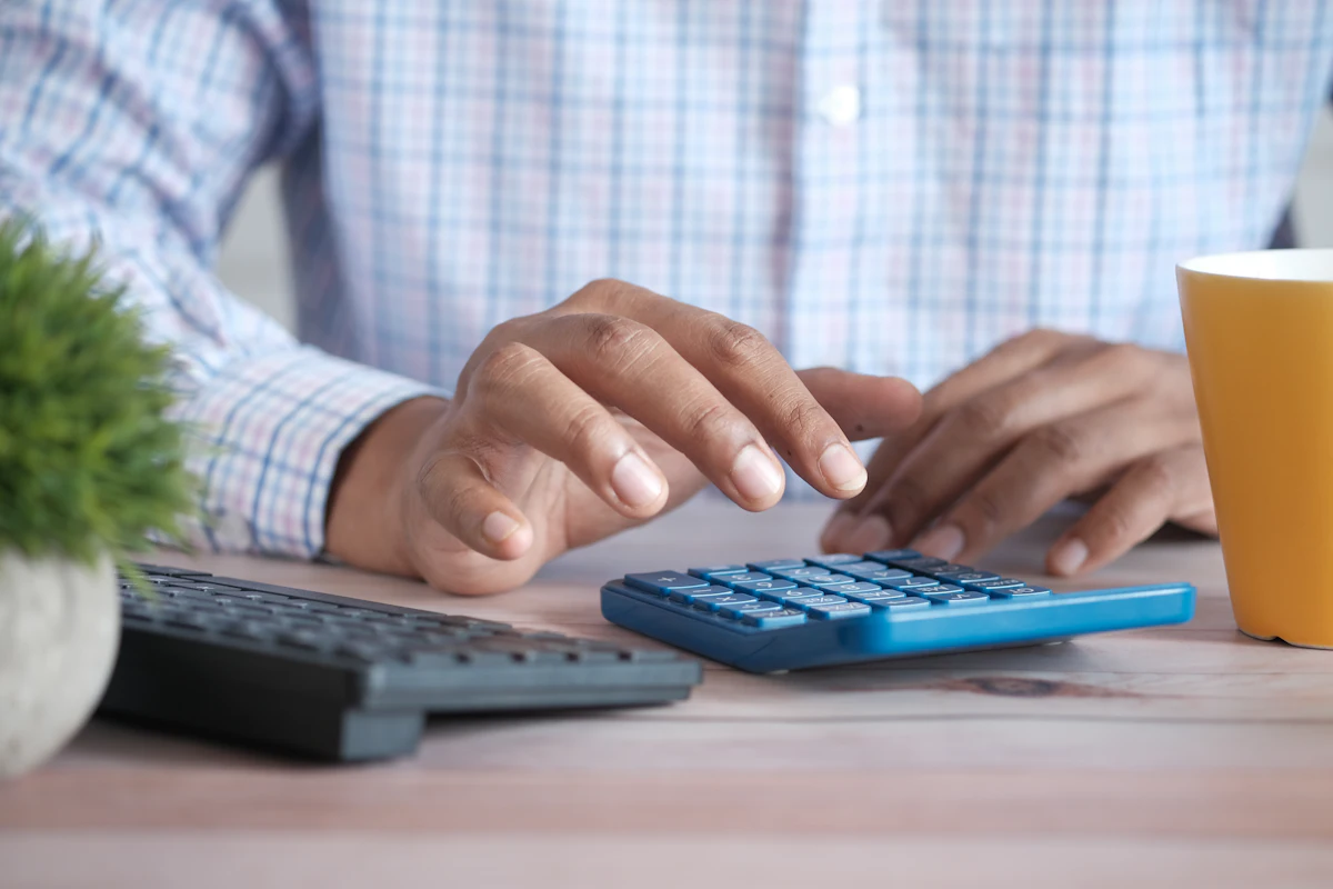 Close-up of hands using a calculator on a desk next to a coffee mug.
