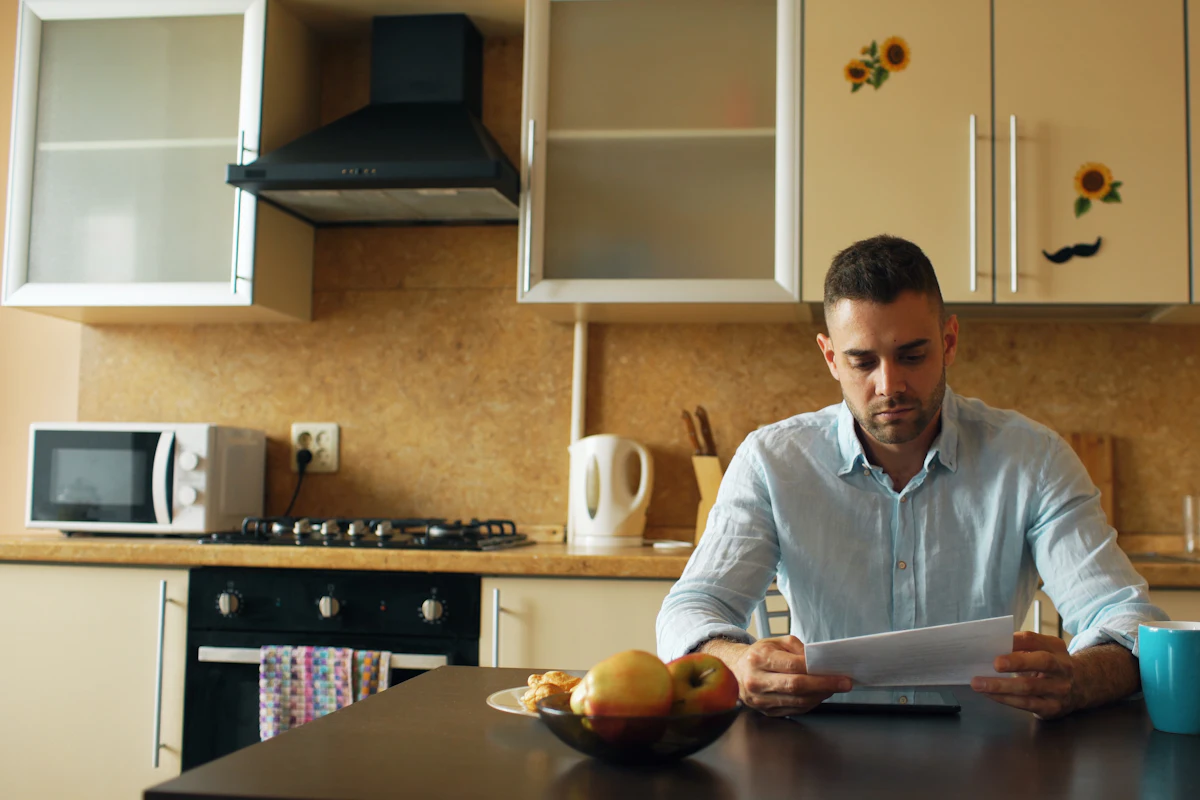 A man at his kitchen table reading a letter over coffee.